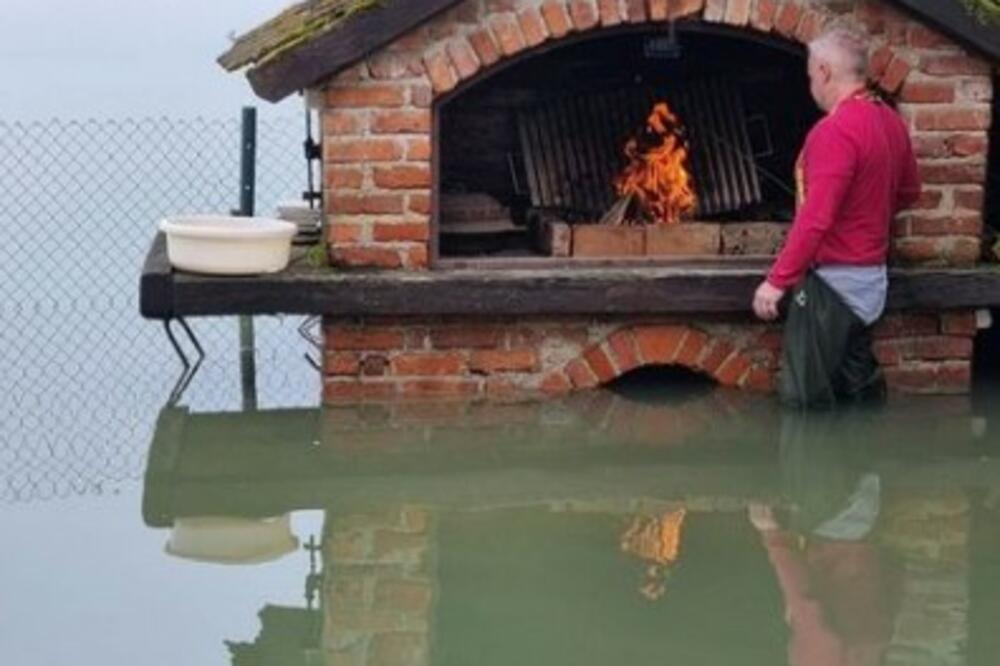 U POPLAVLJENOM DVORIŠTU POTPALIO ROŠTILJ: Hit fotka iz Karlovca, sprema ručak u ribarskim čizmama i vodi do kolena (FOTO)